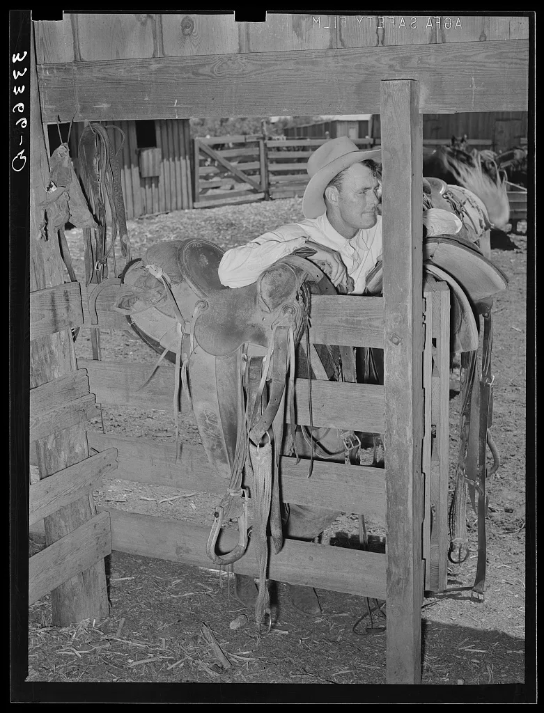 Cowboy leaning on saddle. Saddle room on SMS Ranch near Spur, Texas, 1939