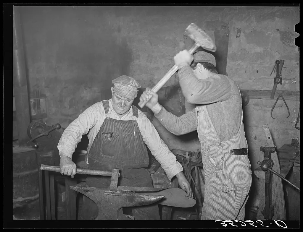 Blacksmith and helper pounding out plow point. Depew, Oklahoma, 1940