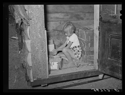 Daughter of homesteader getting chicken feed in slab shed. Trunk seen…, New Mexico, 1940