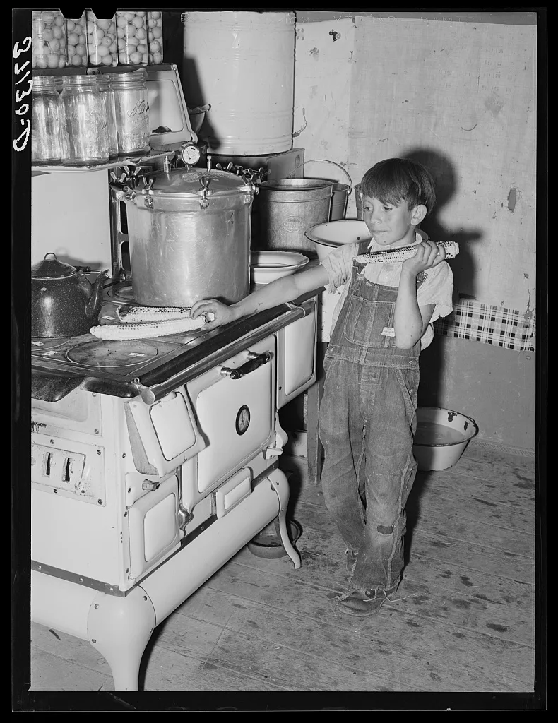 Spanish-American boy eating sweet corn which he has roasted on top of…, New Mexico, 1940